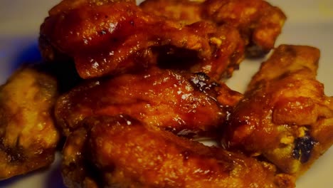 BBQ-chicken-wings-on-a-plate-piled-up-saucy-drums-zoom-in-closeup-white-ceramic-plate-in-a-pub-with-yellow-lights