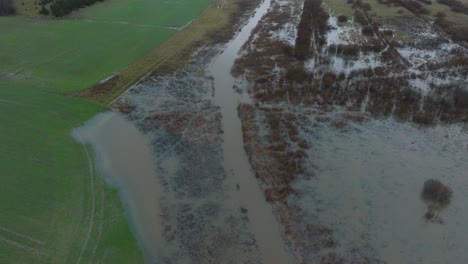 Aerial-establishing-view-of-high-water-in-springtime,-Alande-river-flood,-brown-and-muddy-water,-agricultural-fields-under-the-water,-overcast-day,-wide-drone-shot-moving-forward-tilt-down