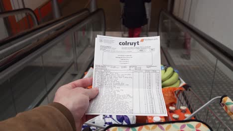 POV-male-hand-checks-supermarket-receipt-after-buying-groceries-in-the-Colruyt-warehouse---Brussels,-Belgiul