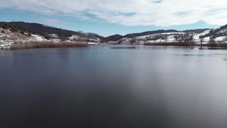 Drone-video-over-frozen-mountain-lake-sunny-winter-day-snow-covered-scenery