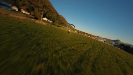 Aerial-tracking-shot-showing-paraglider-landing-in-valley-of-Norway-Fjord-during-sunset-time
