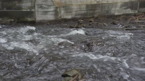 Fast-river-current-flowing-over-rocks-below-concrete-sluice-wall