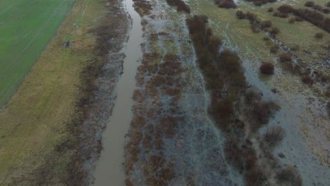 Aerial-establishing-view-of-high-water-in-springtime,-Alande-river-flood,-brown-and-muddy-water,-agricultural-fields-under-the-water,-overcast-day,-wide-drone-shot-moving-forward-tilt-up
