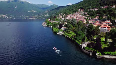 Aerial-orbit-small-boat-cruising-past-Torno-on-Lake-Como,-Italy