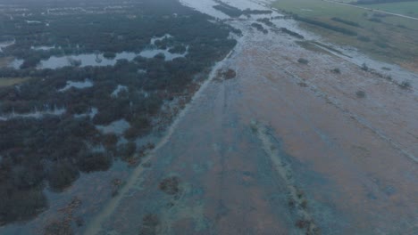 Aerial-establishing-view-of-high-water,-Durbe-river-flood,-brown-and-muddy-water,-agricultural-fields-under-the-water,-overcast-winter-day-with-light-snow,-birdseye-drone-shot-moving-forward