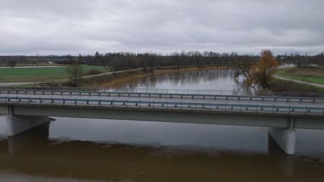Aerial-establishing-view-of-high-water-in-springtime,-Barta-river-flood,-brown-and-muddy-water,-overcast-day,-wide-ascending-drone-shot-moving-forward-over-the-concrete-bridge