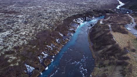 Impressive-drone-shot-of-Hraunfossar-waterfall-and-blue-river-in-vast-volcanic-landscape