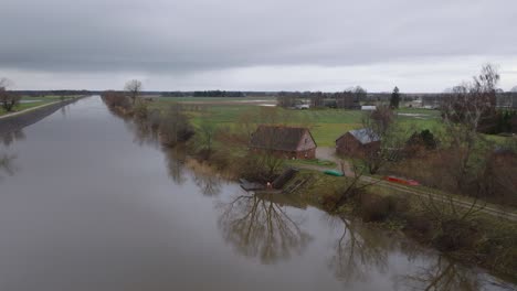 Aerial-establishing-view-of-high-water-in-springtime,-Barta-river-flood,-brown-and-muddy-water,-overcast-day,-remote-house-on-the-bank-of-the-river,-wide-ascending-drone-shot-moving-backward