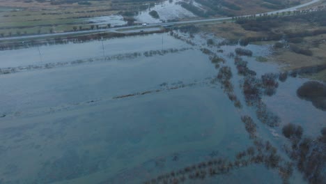 Aerial-establishing-view-of-high-water,-Durbe-river-flood,-brown-and-muddy-water,-agricultural-fields-under-the-water,-overcast-winter-day-with-light-snow,-drone-shot-moving-forward-tilt-down