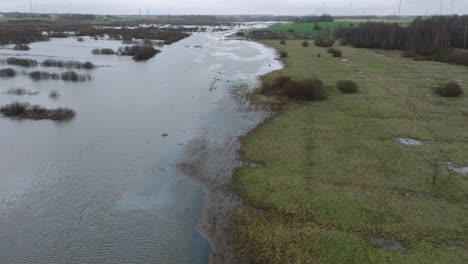 Aerial-establishing-view-of-high-water-in-springtime,-Alande-river-flood,-brown-and-muddy-water,-agricultural-fields-under-the-water,-overcast-day,-wide-drone-shot-moving-forward,-tilt-down
