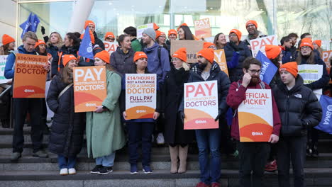 Junior-Doctors-wearing-orange-British-Medical-Association-hats,-hold-orange-placards-on-a-picket-line-outside-the-entrance-of-the-University-College-London-Hospital-on-the-26th-day-of-strike-action