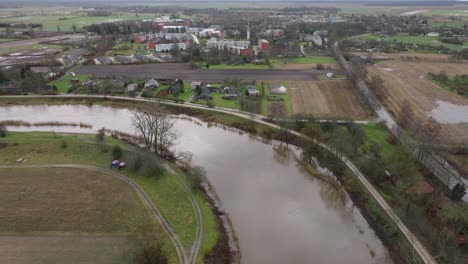 Aerial-establishing-view-of-high-water-in-springtime,-Barta-river-flood,-brown-and-muddy-water,-overcast-day,-wide-drone-shot-moving-forward,-tilt-down