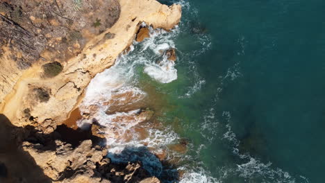 Raveling-aerial-of-the-rugged-coastline-of-Portugal-unfolds,-as-the-gentle-sea-waves-delicately-embrace-the-rocky-formations-under-the-radiant-sunshine-of-a-delightful-day