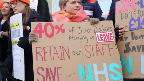 In-slow-motion-a-woman-holds-a-handmade-cardboard-placard-that-reads,-“40%-of-Junior-Doctors-planning-to-leave