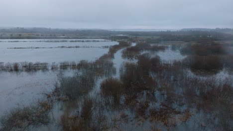 Aerial-establishing-view-of-high-water,-Durbe-river-flood,-brown-and-muddy-water,-agricultural-fields-under-the-water,-overcast-winter-day-with-light-snow,-wide-drone-shot-moving-forward-low