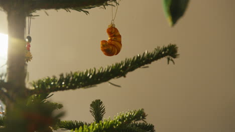 Golden-croissant-ornament-dangling-from-a-lush-Christmas-tree