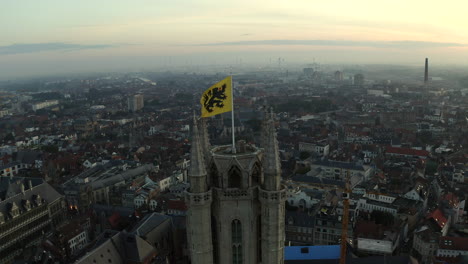 Aerial-Parallax-shot-of-Old-Bell-Tower-with-Flag-of-Flanders,-Ghent,-Belgium