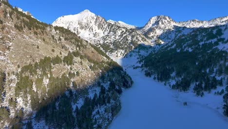 Drohnenaufnahmen-Eines-Eisigen-Tals-Mit-Einem-Zugefrorenen-See-Und-Bäumen-Unter-Dem-Schnee-In-Den-Pyrenäen