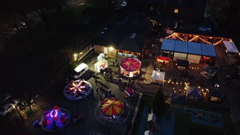 Illuminated-Christmas-fairground-festival-in-neighbourhood-car-park-at-night-aerial-view