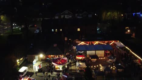 Illuminated-Christmas-funfair-in-neighbourhood-pub-car-park-at-night-aerial-reveal-view