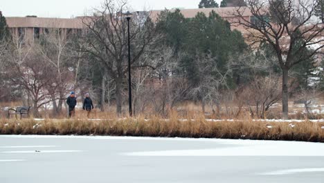 Couple-Walking-on-Path-in-Park-With-Frozen-Lake-in-Colorado