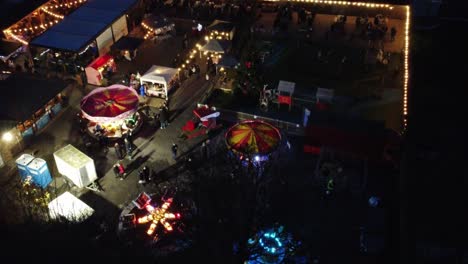 Illuminated-Christmas-fairground-festivities-in-neighbourhood-pub-car-park-at-night-aerial-view
