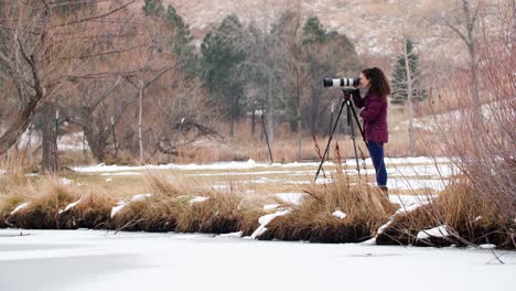 Woman-Photographer-Taking-Pictures-with-Camera-at-Frozen-Lake-in-Colorado-Park