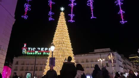 Menschen-Werden-Gesehen,-Wie-Sie-Während-Der-Weihnachtsfeiertage-Auf-Dem-Platz-Puerta-Del-Sol-In-Madrid-Eine-Beleuchtete-Weihnachtsbauminstallation-Genießen,-Die-Mit-Goldenen-LED-Lichtern-Geschmückt-Ist