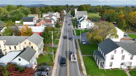 Aerial-pullback-reveal-of-traditional-1900s-community-homes-along-rural-road-in-USA-rolling-hills-during-autumn