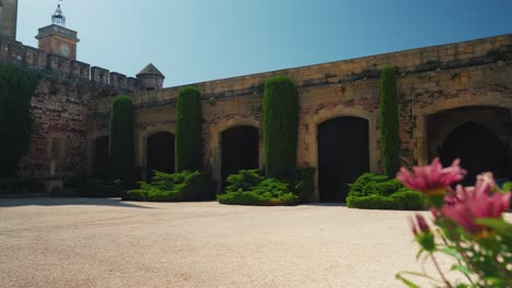 Puertas-De-Entrada-De-Un-Gran-Castillo-Medieval-En-Pouzilhac,-Pintoresco-Jardín-Con-Plantas-Y-Flores-En-Un-Día-Claro