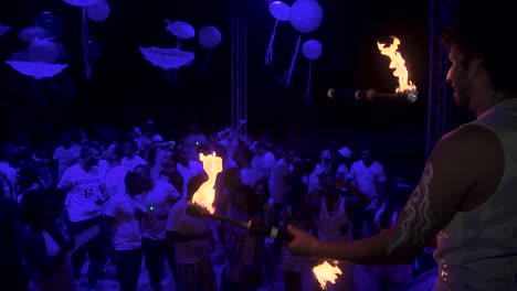 Juggling-Man-with-fire-Torches-in-the-Nightclub-while-watching-the-Dance-Floor-full-of-People-Dancing-in-the-Background,-Slowmotion
