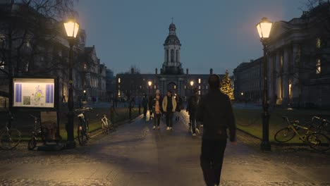 Estudiantes-Caminando-A-La-Entrada-Del-Trinity-College-De-Dublín-Por-La-Noche-Con-Vistas-Al-Campanario-De-Dublín,-Irlanda