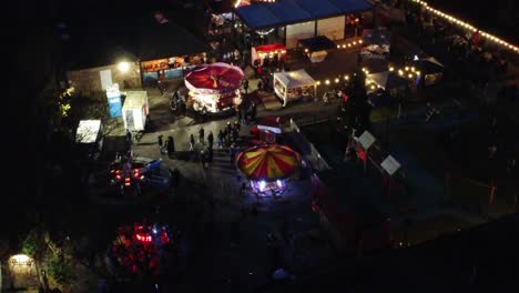Illuminated-Christmas-fairground-event-in-neighbourhood-car-park-at-night-aerial-view