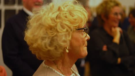 Older-blonde-woman-with-curls-and-modern-frame-responds-to-a-speech