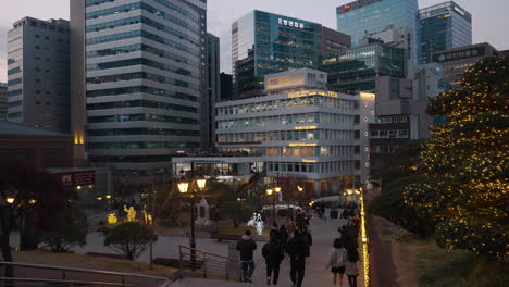 Group-of-People-Sightseeing-Chrismas-Decorations-at-Myeongdong-Cathedral-Park-at-Sunset-with-Seoul-Downtown-Buildings-in-backdrop