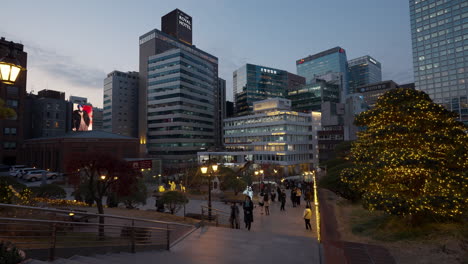 Myeongdong-Cathedral-Park-at-Sunset-with-Seoul-Urban-Skyline-in-backgound,-People-Walking