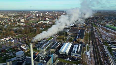 Steaming-factory-near-small-township-in-early-winter,-aerial-view