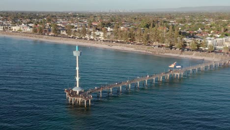 Aerial-of-Brighton-beach-jetty-with-Adelaide-CBD-in-background,-South-Australia