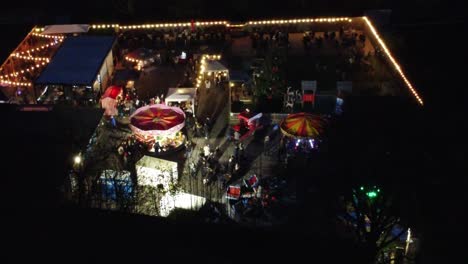 Illuminated-colourful-Christmas-fairground-festival-in-neighbourhood-car-park-at-night-aerial-view
