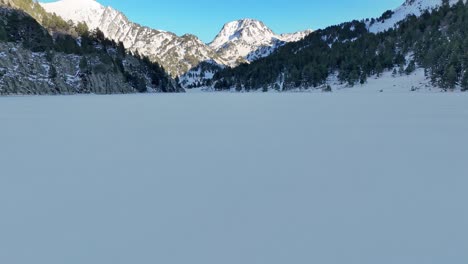 Drone-footage-on-a-frozen-lake,-revealing-distant-mountains-in-the-Pyrenees-mountains