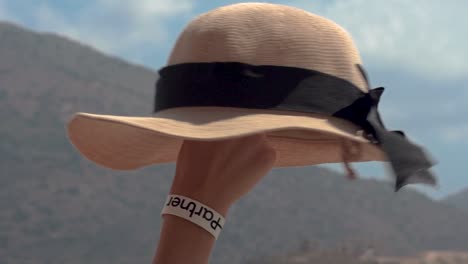 Woman's-Arm-with-Partner-Logo-Festival-Bracelet-Spinning-a-Straw-Hat-with-her-Finger,-Mountainous-Background,-Slowmotion