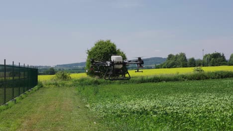 Landwirtschaftliche-Drohne-Mit-Wassertank-Und-Sprühsystem-Schwebt-über-Grünem-Ackerland