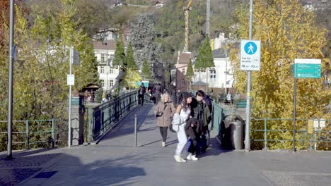 People-walking-across-a-pedestrian-bridge-on-a-sunny-day-in-autumn-in-the-heart-of-Meran---Merano,-South-Tyrol,-Italy