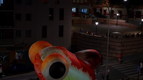 Colorful-fish-balloon-leaking-helium-and-falling-on-people-heads-at-night