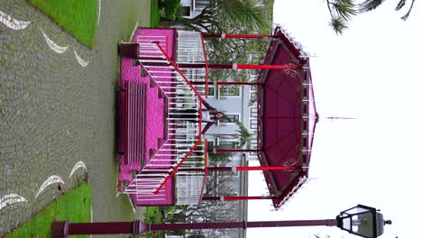 Joyful-woman-raising-her-arms-in-pink-kiosk-at-Duke-of-Terceira-Garden,-Portugal