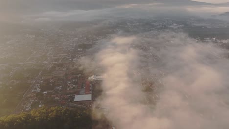 Foggy-morning-at-Antigua-city-with-volcano-agua-in-background,-aerial