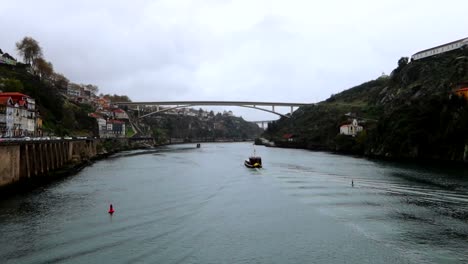 Boat-navigating-in-Douro-River-towards-Ponte-Infante-Dom-Henrique-on-a-cloudy-day