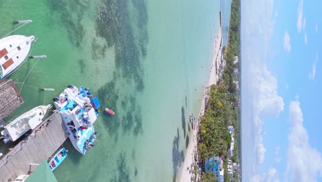 Picturesque-tropical-Caribbean-beach-with-docked-tourist-boats,-vertical-aerial