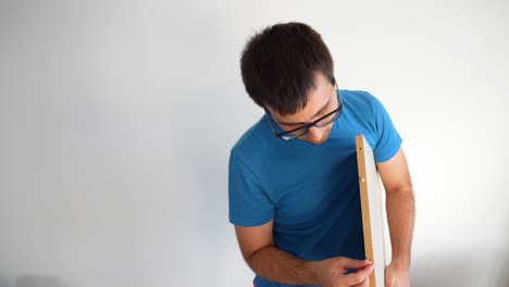 Young-man-installing-wooden-plugs-into-white-plank-of-furniture,-medium-front-shot