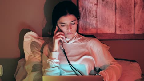 Young-woman-multitasking-with-phone-and-laptop-in-bed